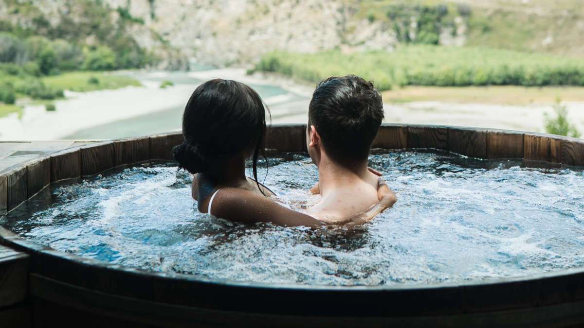 Pärchen in einem kleinen Pool umarmen sich und schauen in die bergige Landschaft im Hintergrund.