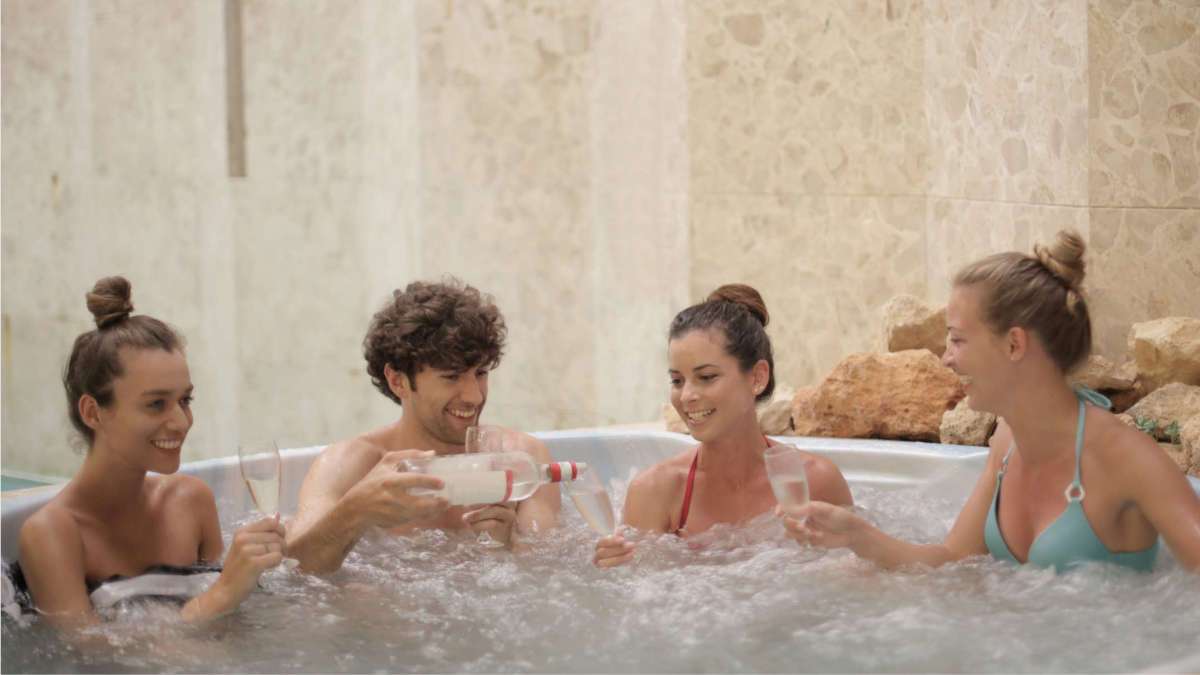 3 Frauen und 1 Mann füllen Sekt ein in einem Pool.