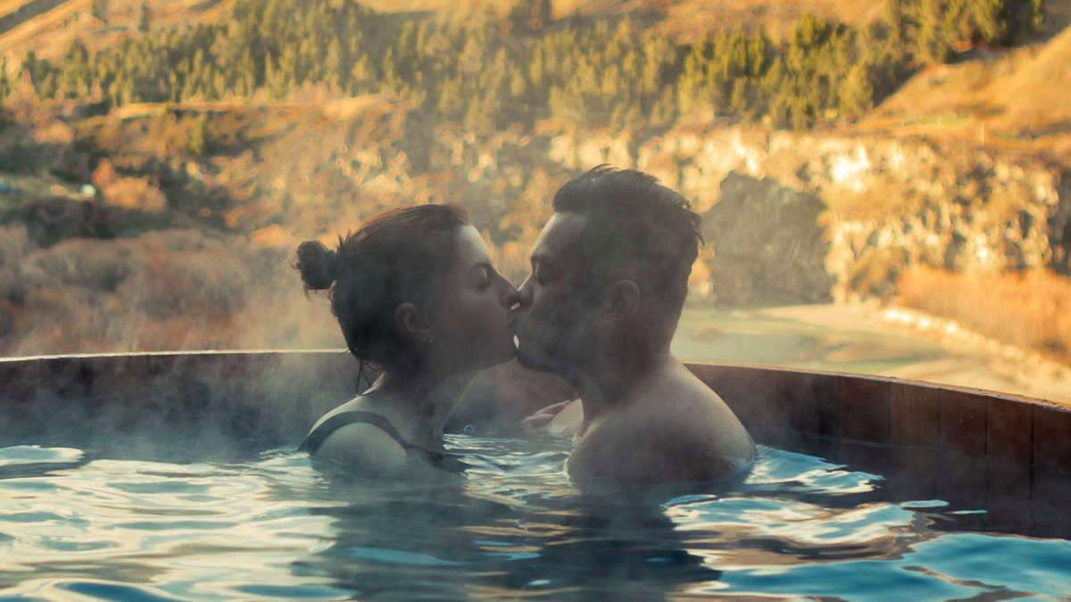 Küssendes Pärchen im Pool vor einem bergigen Hintergrund.